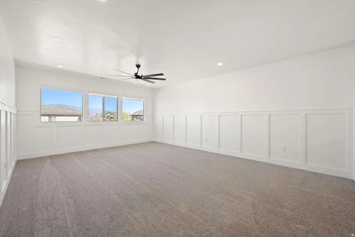 Empty room featuring a decorative wall, wainscoting, ceiling fan, and carpet floors