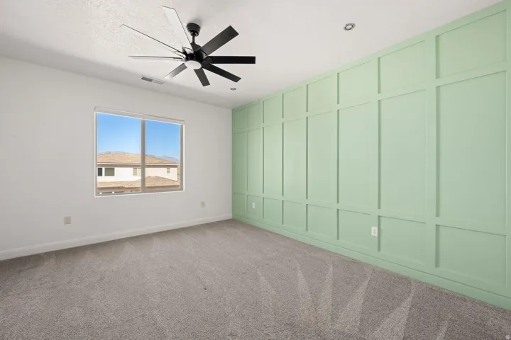 Spare room featuring a decorative wall, light colored carpet, and a ceiling fan