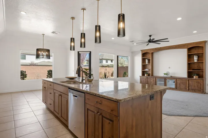 Kitchen with dark stone countertops, dishwasher, a center island with sink, decorative light fixtures, and healthy amount of natural light
