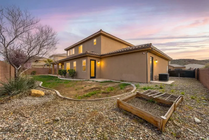Back of property at dusk with a fenced backyard, a patio area, a vegetable garden, and stucco siding