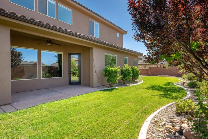 Expansive backyard featuring a manicured lawn, established landscaping, and a covered patio with a ceiling fan
