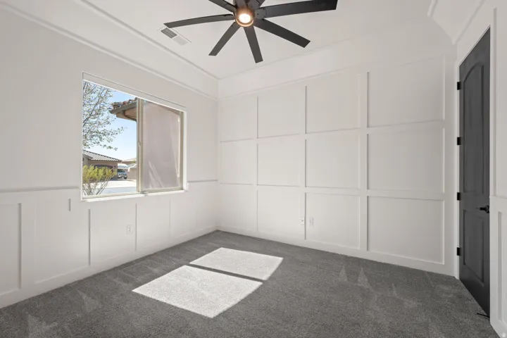Unfurnished bedroom featuring a decorative wall, ceiling fan, a wainscoted wall, and dark carpet
