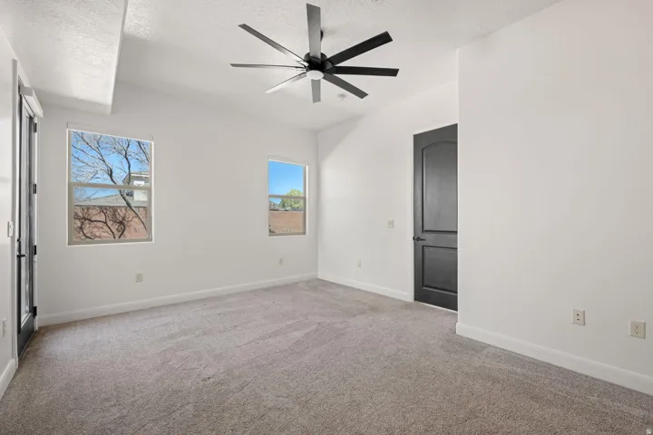 Empty room with light colored carpet, a textured ceiling, and a ceiling fan