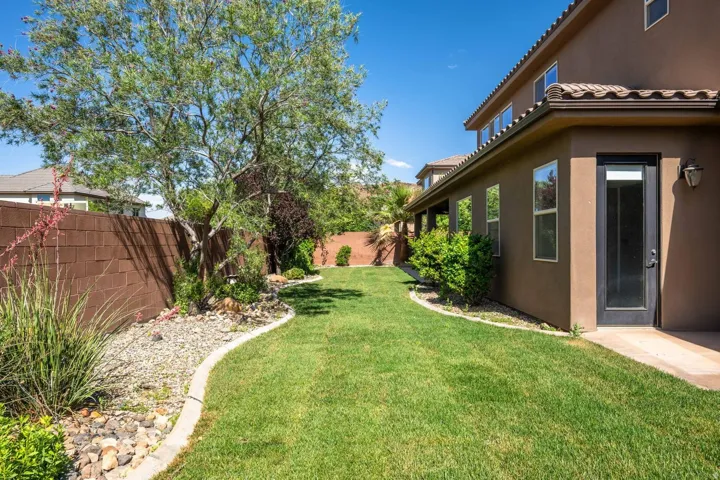 Expansive green lawn with established landscaping, featuring a mature tree, decorative rock beds, and a block perimeter fence