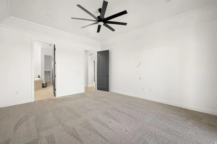 Unfurnished bedroom featuring light carpet, a ceiling fan, and ensuite bathroom