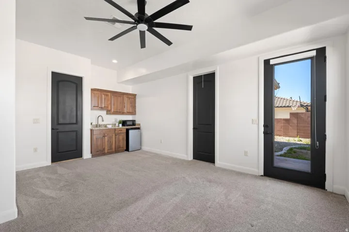 Unfurnished living room featuring light carpet, bar with sink, and a ceiling fan