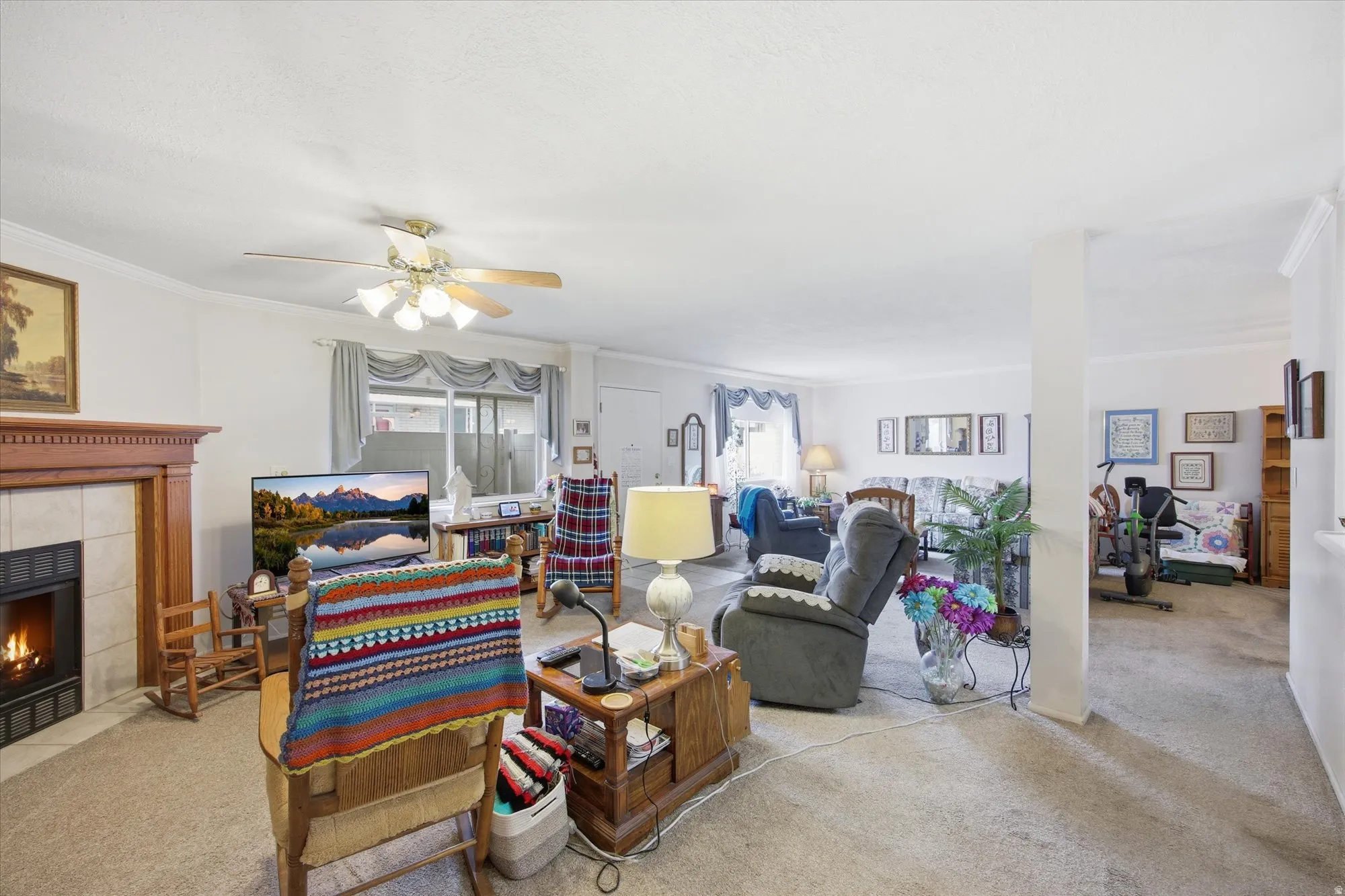 Living area with light colored carpet, a tile fireplace, crown molding, and a ceiling fan