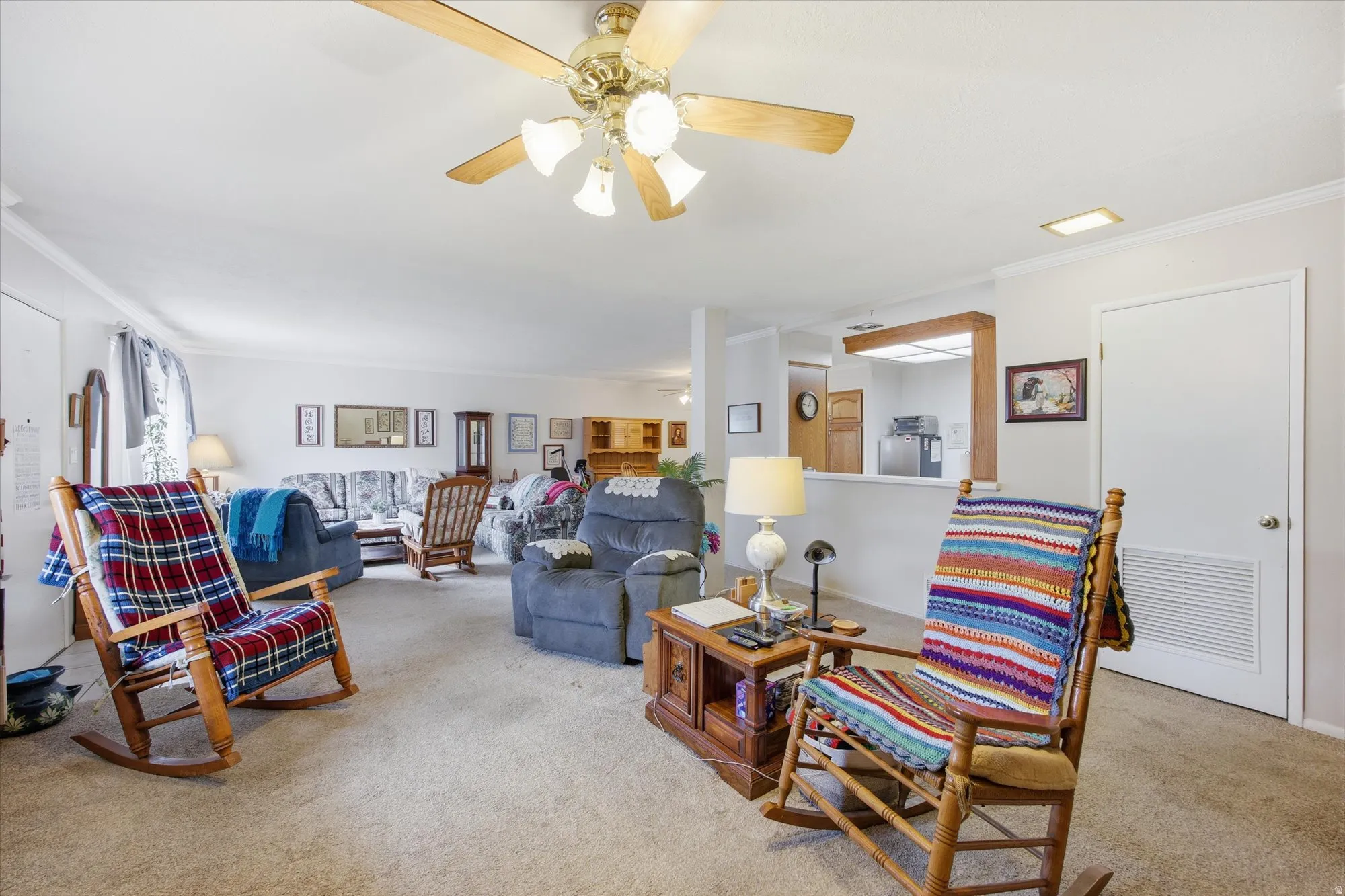 Carpeted living area with crown molding and ceiling fan
