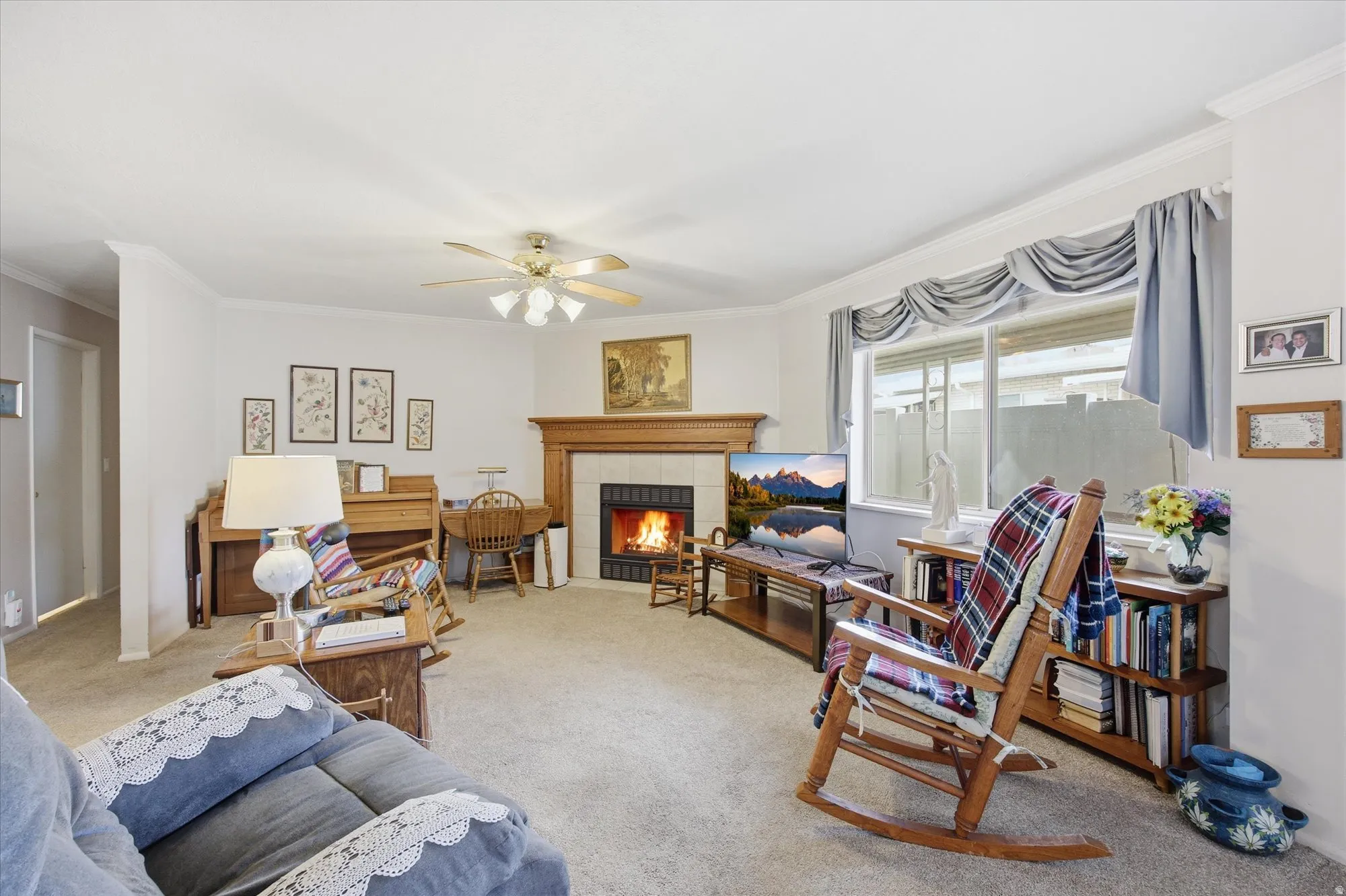 Living area featuring crown molding, a tiled fireplace, a ceiling fan, and light carpet