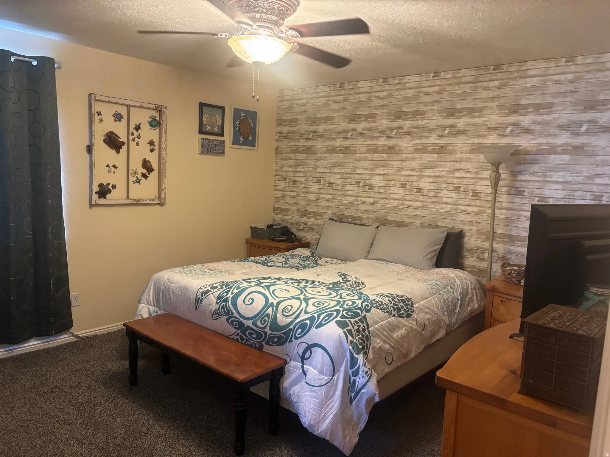 Bedroom featuring ceiling fan, carpet, a textured ceiling, an accent wall, and wooden walls