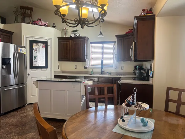 Kitchen with stainless steel appliances, dark wood finish cabinets, light countertops, suspended lighting, and lofted ceiling