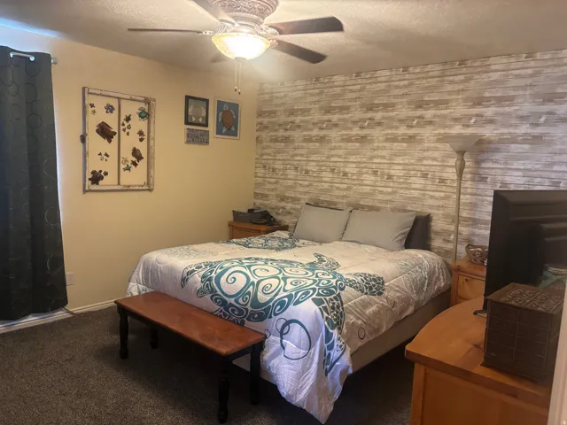 Bedroom featuring ceiling fan, carpet, a textured ceiling, an accent wall, and wooden walls