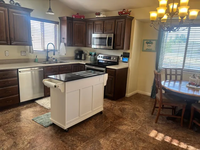 Kitchen with stainless steel appliances, hanging lights, vaulted ceiling, a kitchen island, and dark stone countertops
