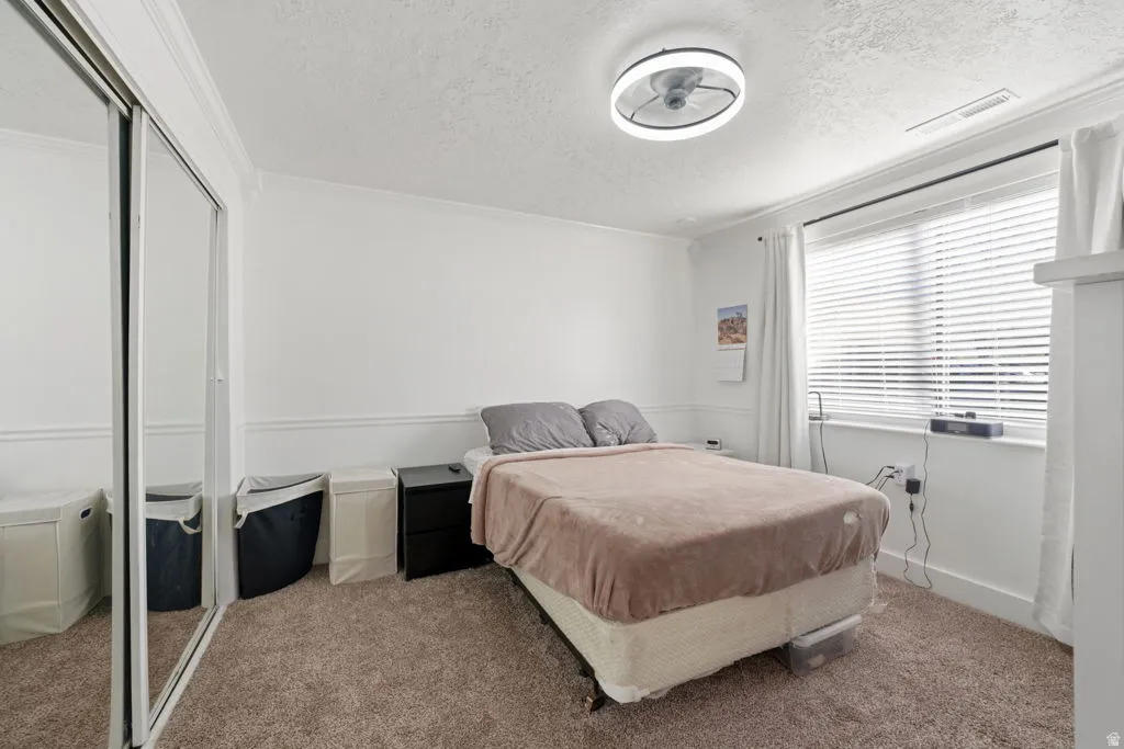 Bedroom with a closet, a textured ceiling, carpet, and crown molding