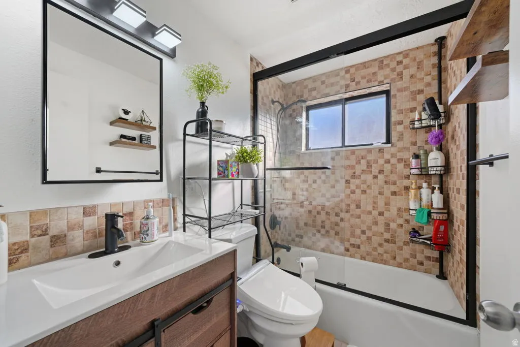 Full bath with vanity, bath / shower combo with glass door, and backsplash