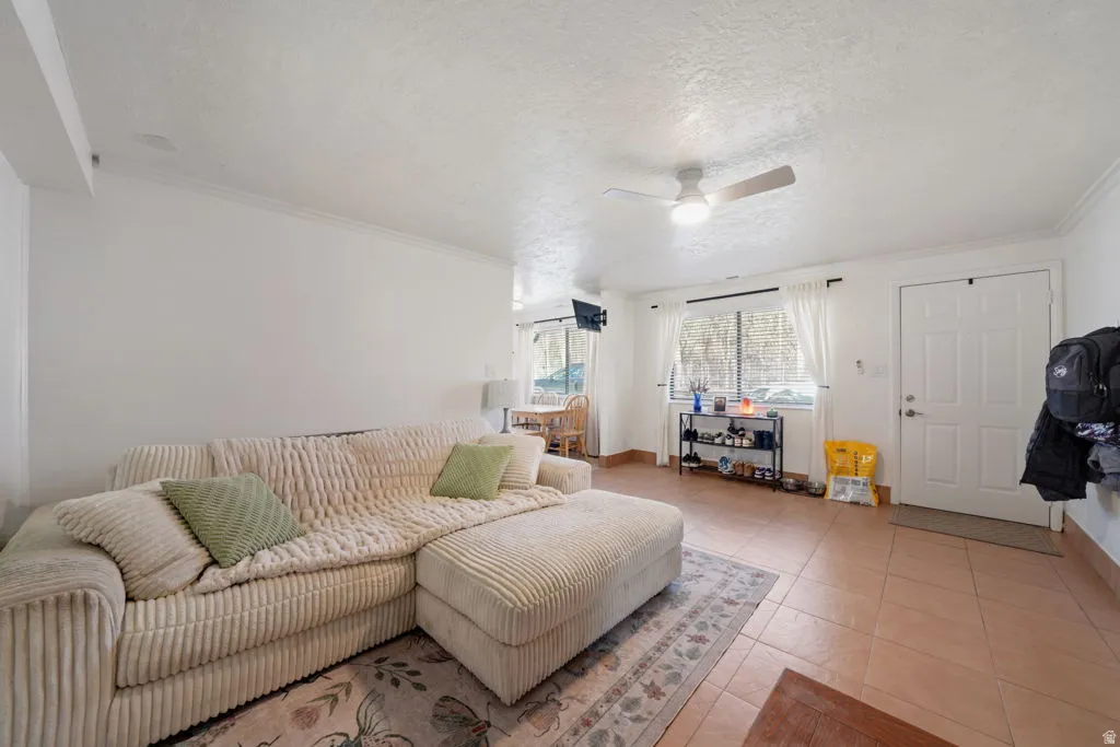 Living room with a textured ceiling, a ceiling fan, light tile patterned floors, and crown molding