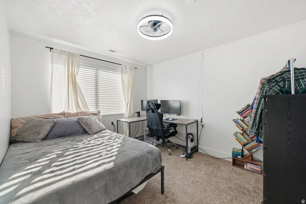 Bedroom with light carpet, a desk, and a textured ceiling