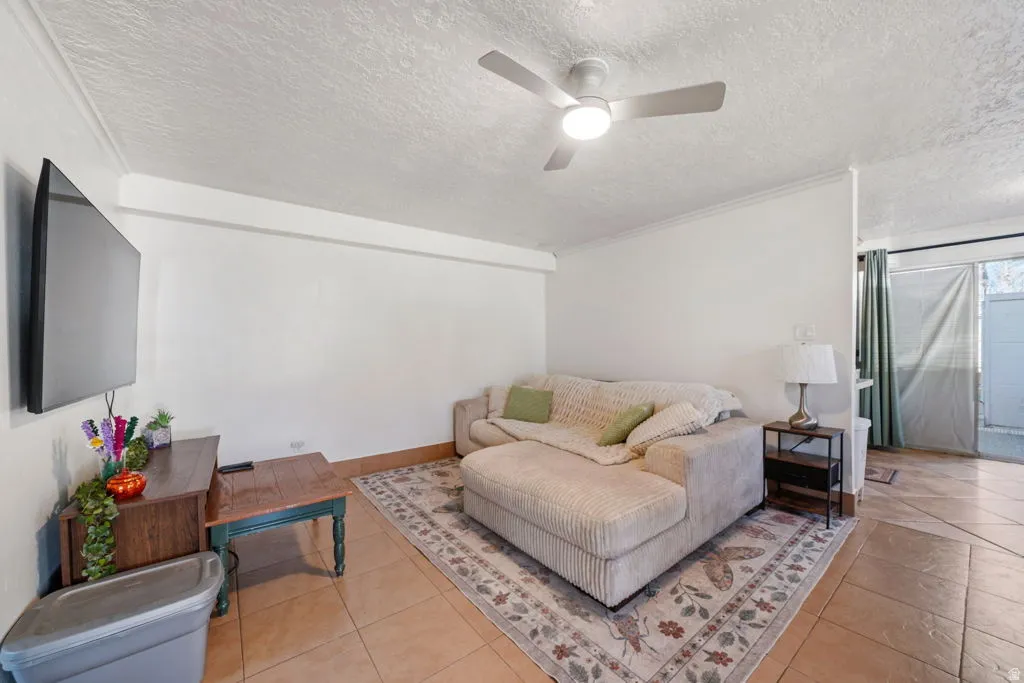 Living area featuring a ceiling fan, a textured ceiling, light tile patterned floors, and crown molding