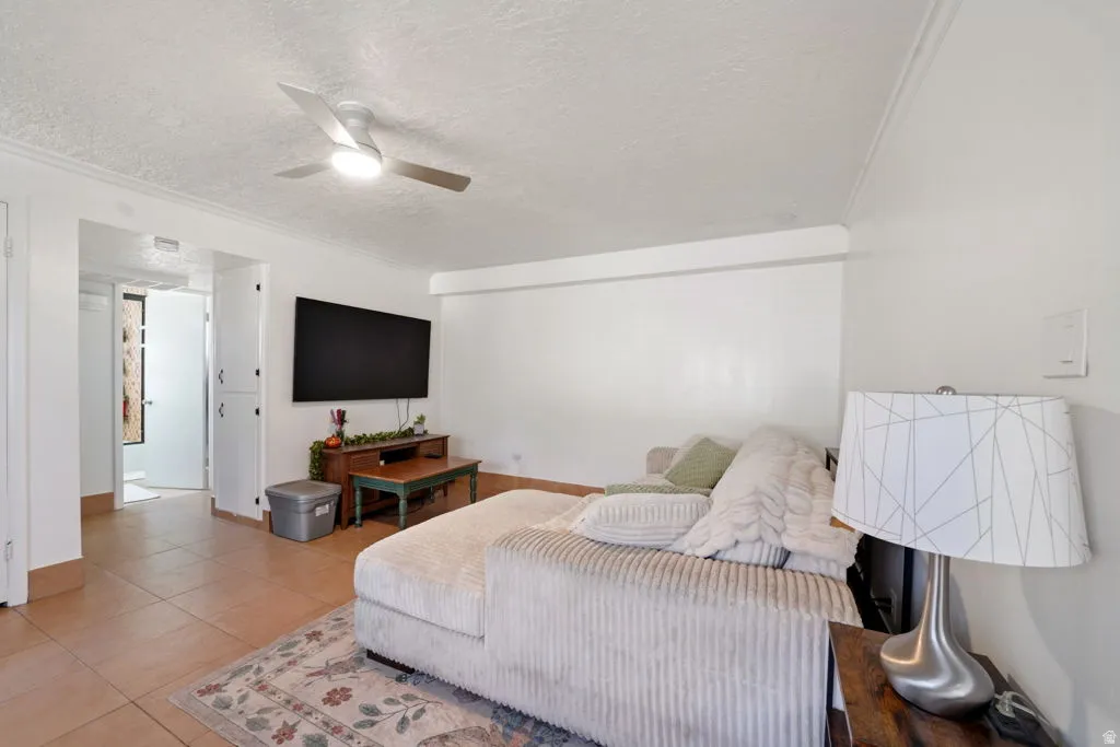 Living room with crown molding, light tile patterned floors, ceiling fan, and a textured ceiling