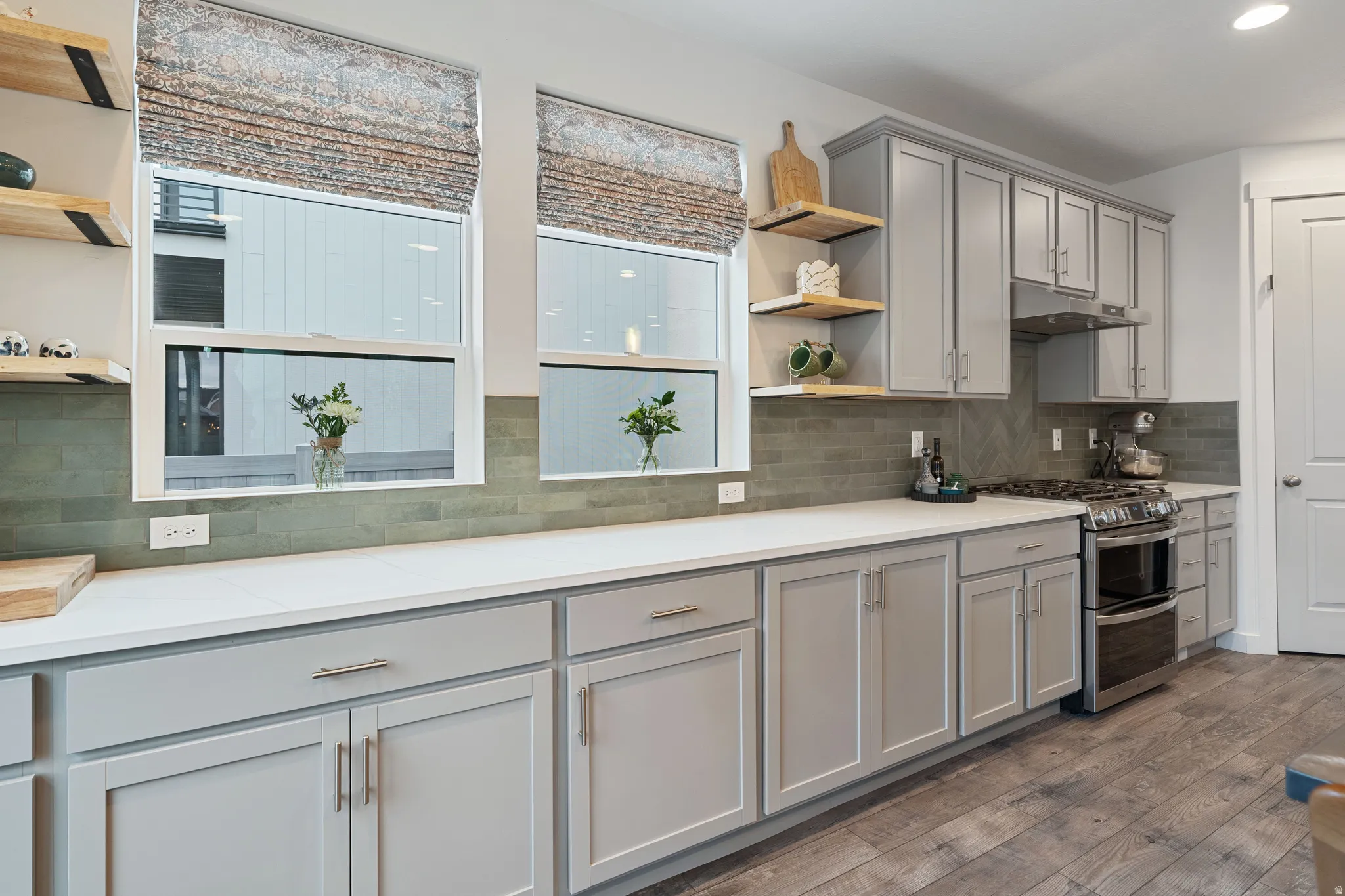 Kitchen featuring open shelves, gray cabinets, double oven range, dark wood-style floors, and light stone countertops