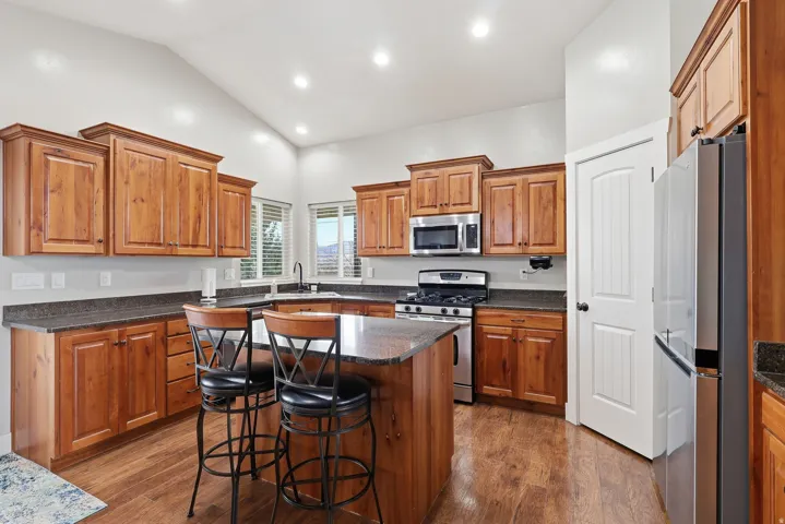 Kitchen featuring wood finish cabinets, stainless steel appliances, a breakfast bar, lofted ceiling, and dark wood-style floors