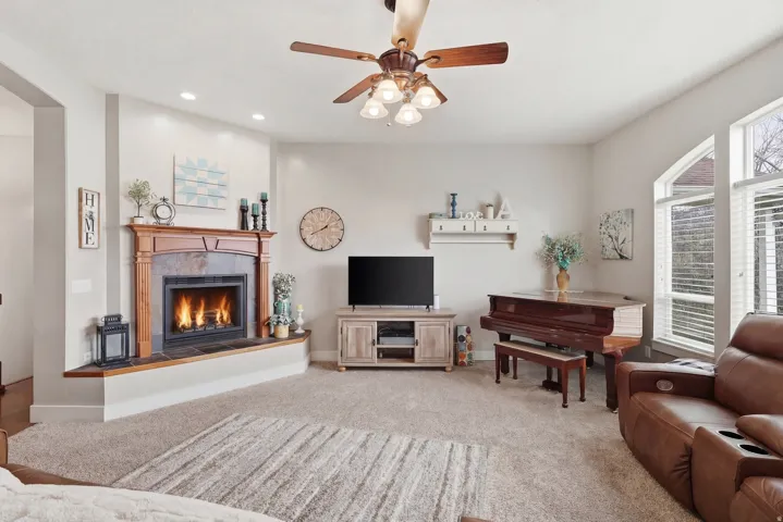 Living area with ceiling fan, a tiled fireplace, and light carpet