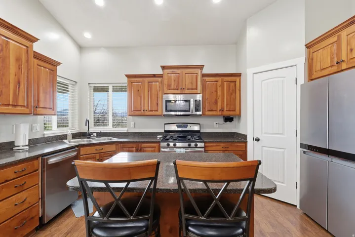 Kitchen with stainless steel appliances, a center island, wood finish cabinetry, a kitchen breakfast bar, and dark stone countertops