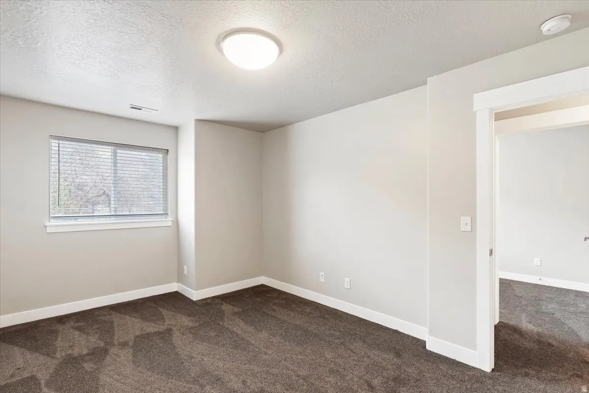 Unfurnished room featuring dark carpet, a textured ceiling, and a smoke detector