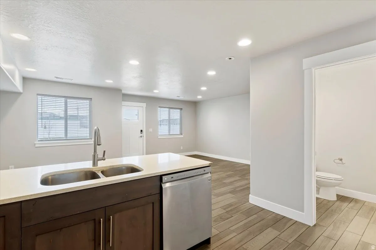 Kitchen with wood tiled floors, dishwasher, dark wood finish cabinetry, light stone countertops, and recessed lighting