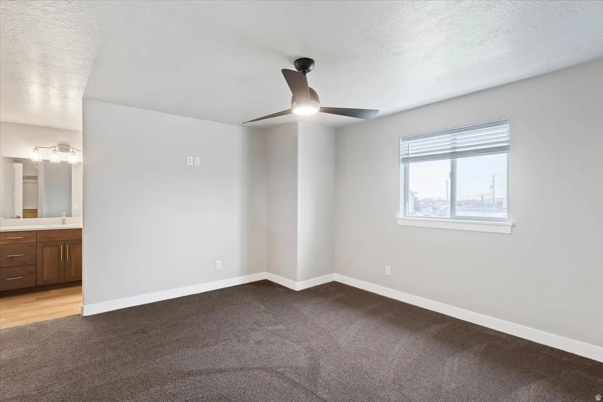 Unfurnished bedroom with dark carpet, a ceiling fan, connected bathroom, and a textured ceiling