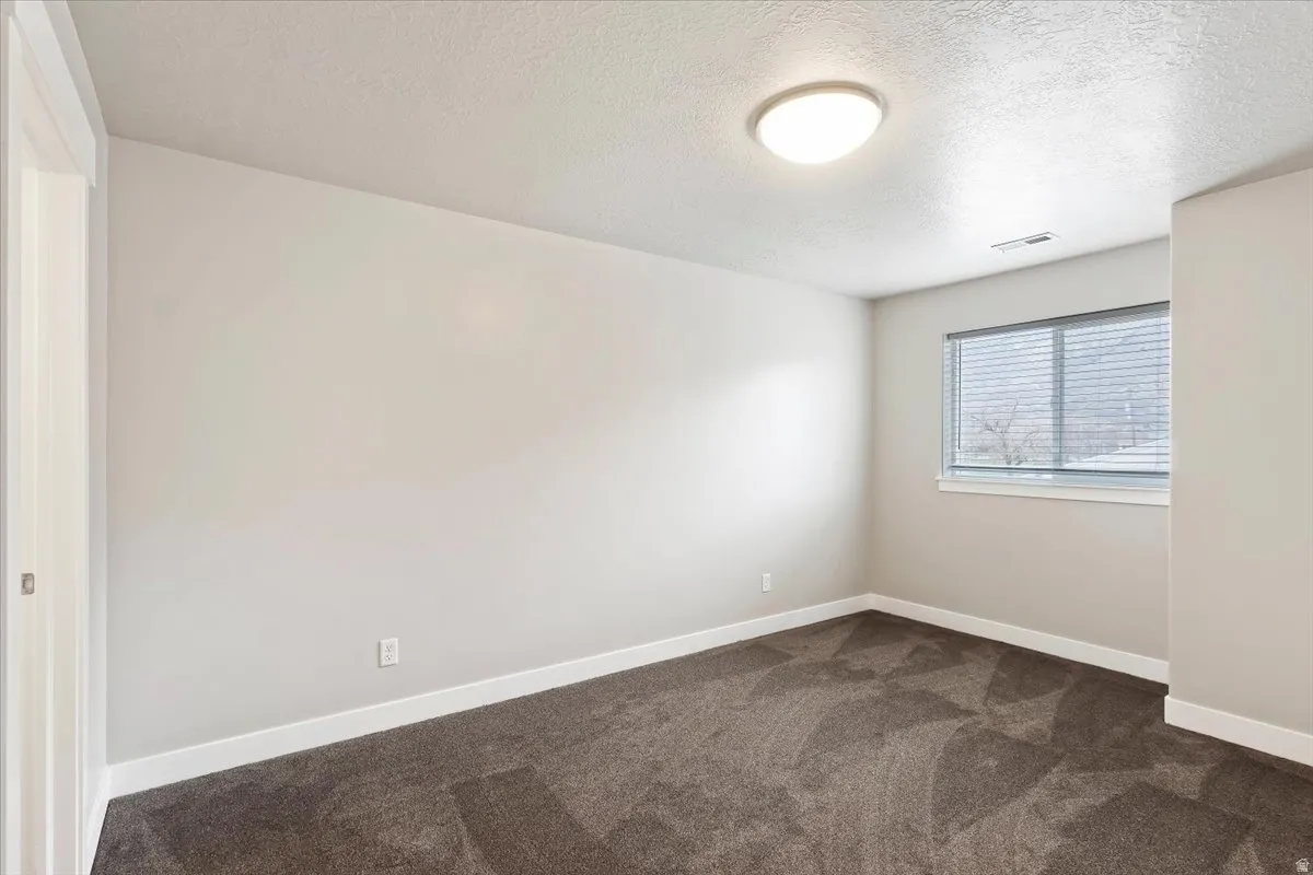 Empty room with a textured ceiling and dark carpet