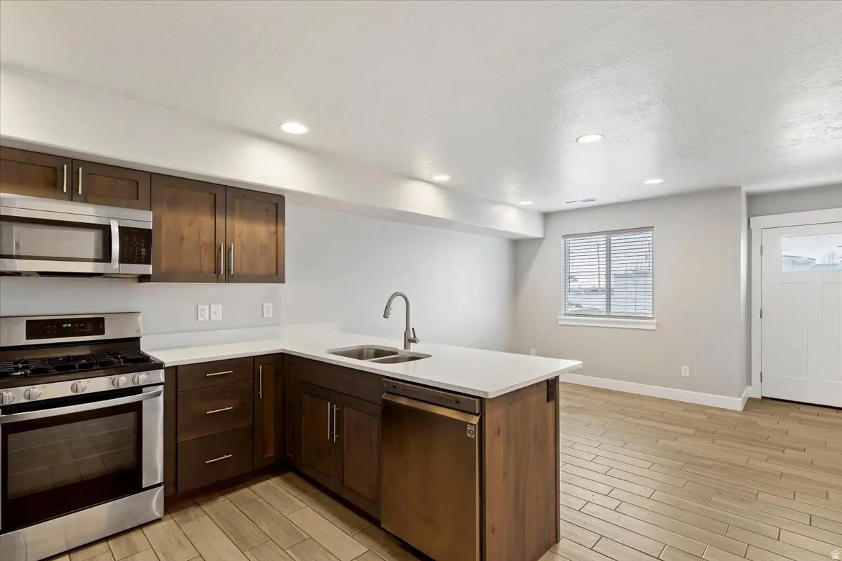 Kitchen featuring stainless steel appliances, a peninsula, dark wood finish cabinetry, wood finish floors, and recessed lighting