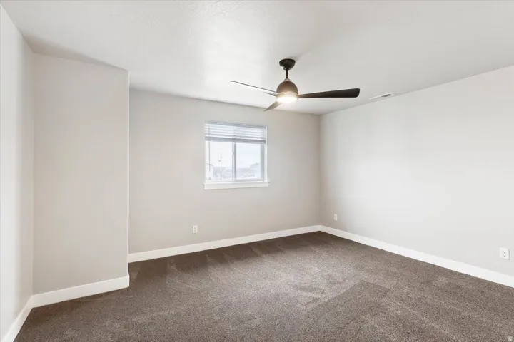 Spare room featuring dark colored carpet and a ceiling fan