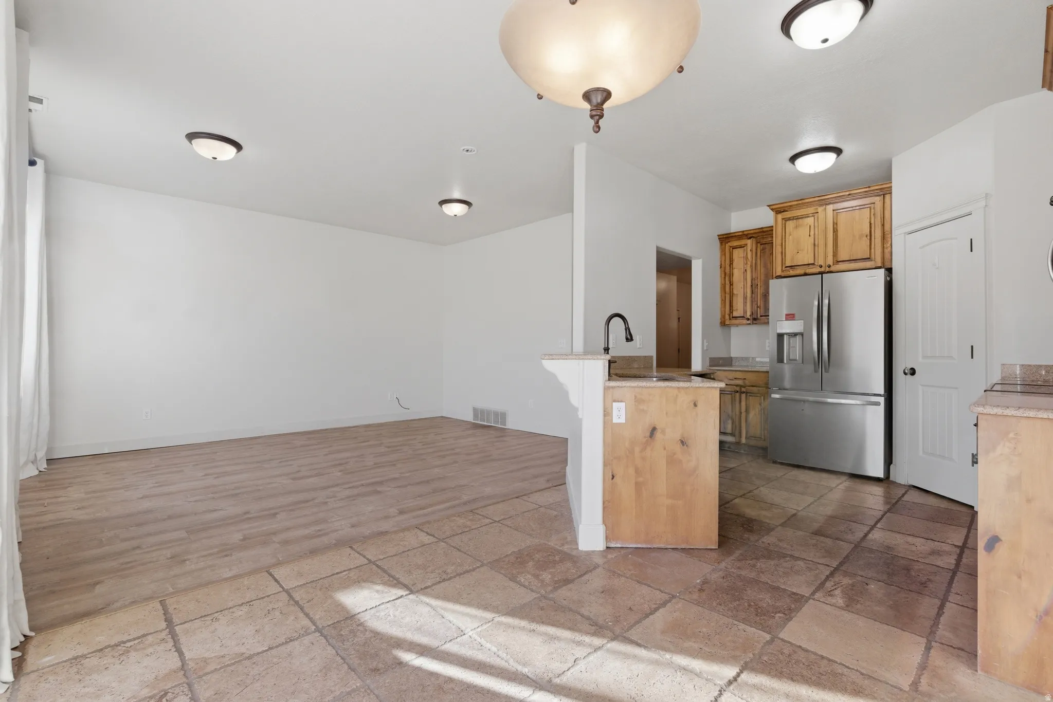 Kitchen featuring stone tile flooring, stainless steel refrigerator with ice dispenser, wood finish cabinetry, a breakfast bar, and a peninsula