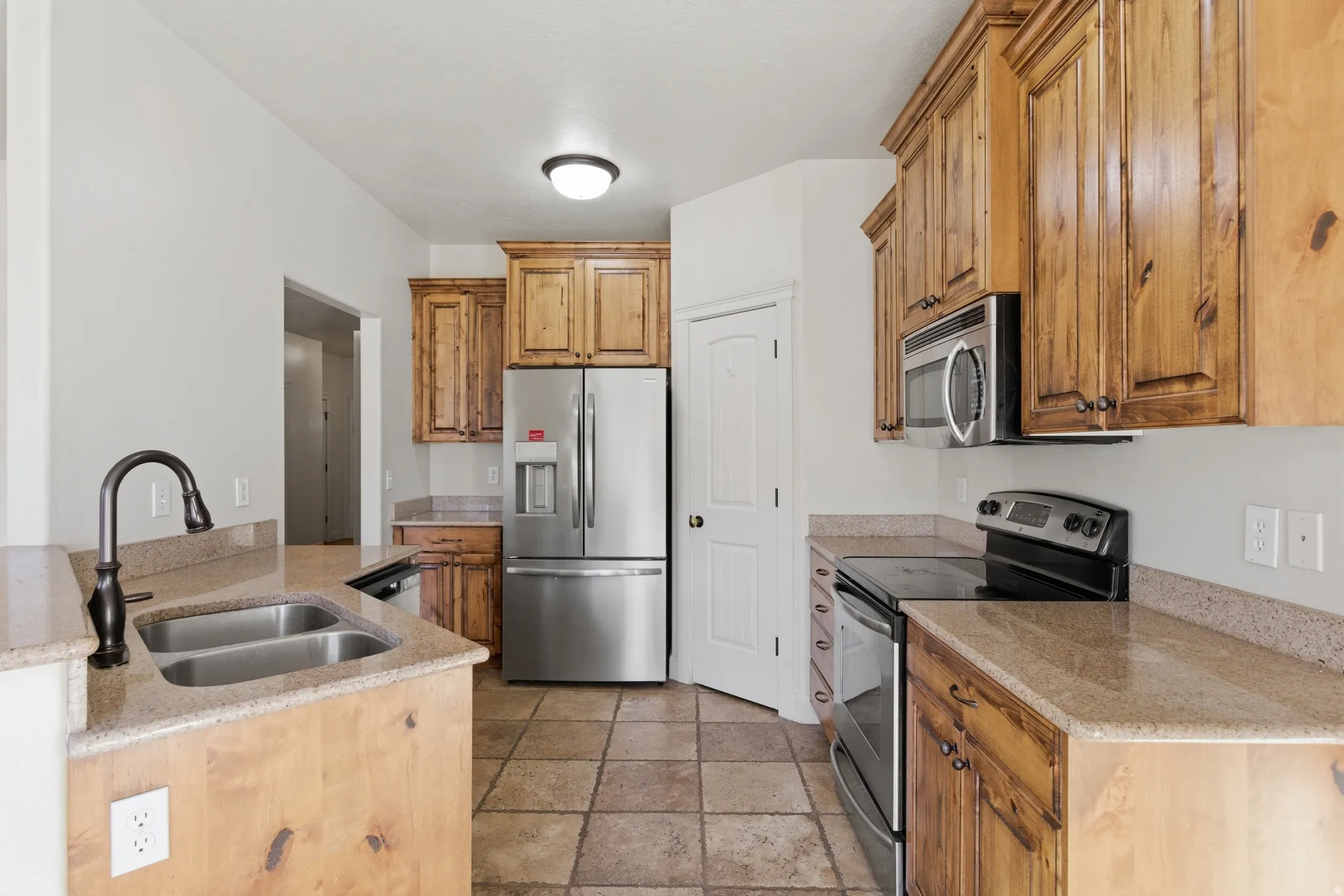 Kitchen featuring stainless steel appliances, light stone counters, wood finish cabinetry, and light stone finish floors