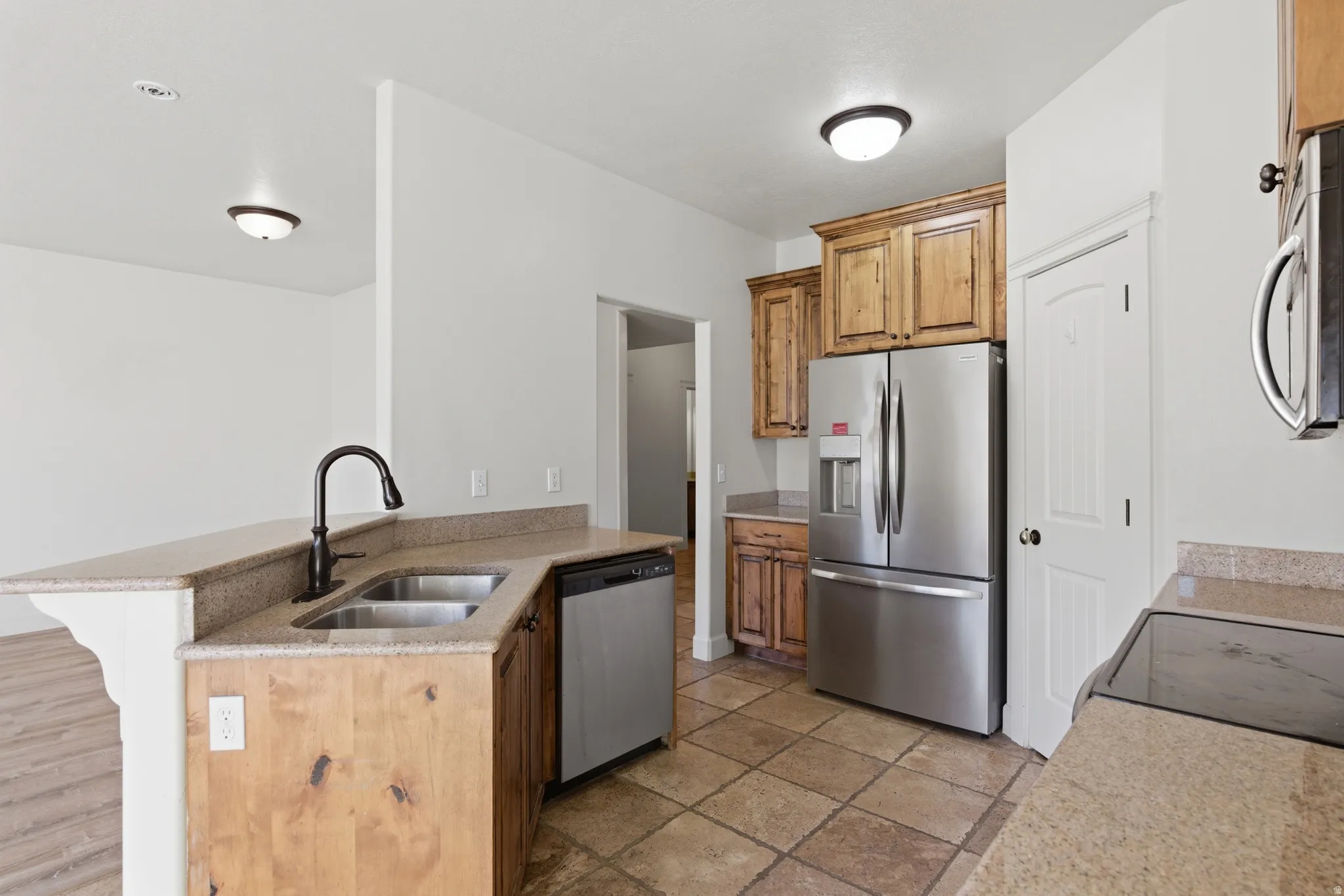 Kitchen featuring stainless steel appliances, a peninsula, light stone countertops, a breakfast bar area, and wood finish cabinetry