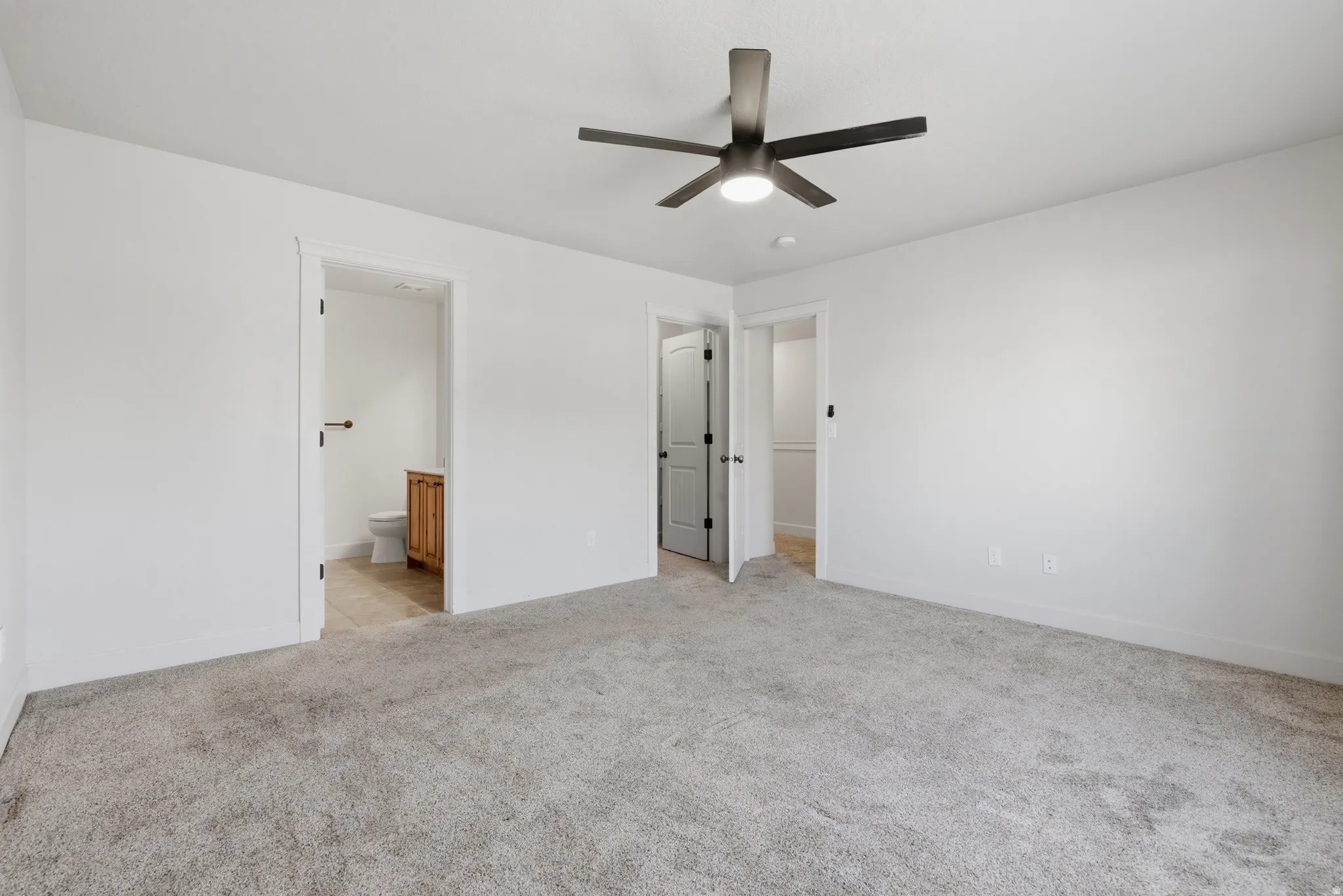 Unfurnished bedroom with light carpet, ceiling fan, and ensuite bathroom