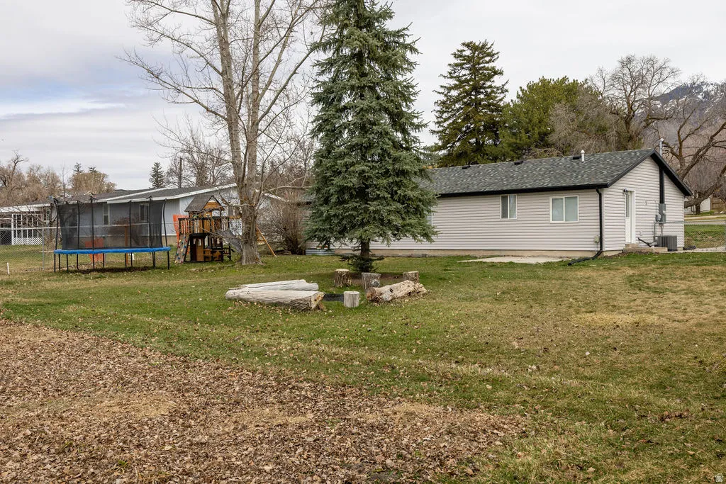View of grassy yard featuring a patio area, a trampoline, and a playground