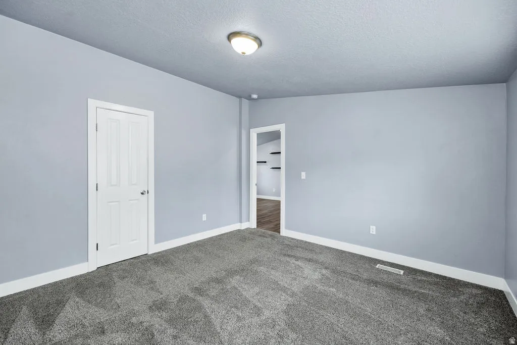 Unfurnished bedroom featuring dark carpet and a textured ceiling