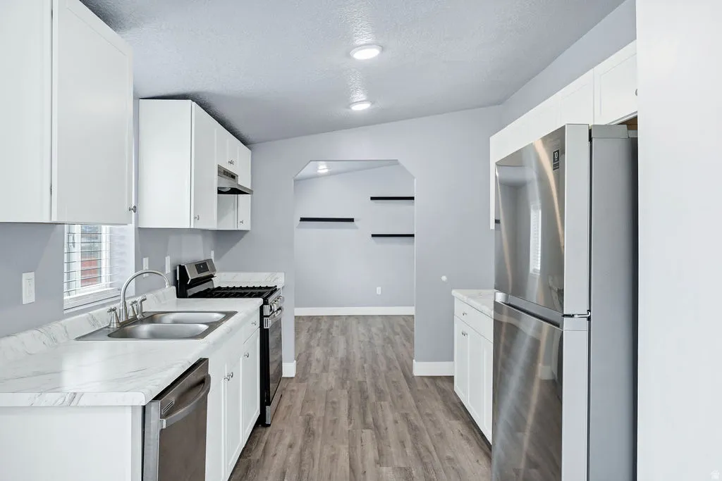 Kitchen featuring stainless steel appliances, light countertops, white cabinets, light wood-type flooring, and a textured ceiling