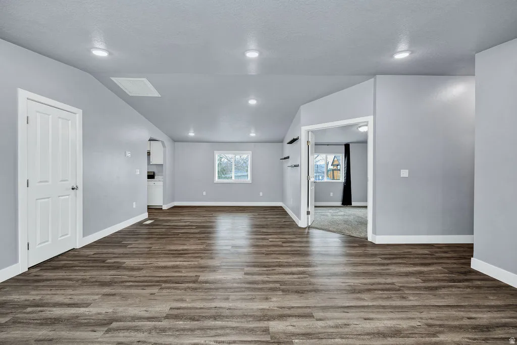 Unfurnished living room with dark wood-style flooring, recessed lighting, and lofted ceiling