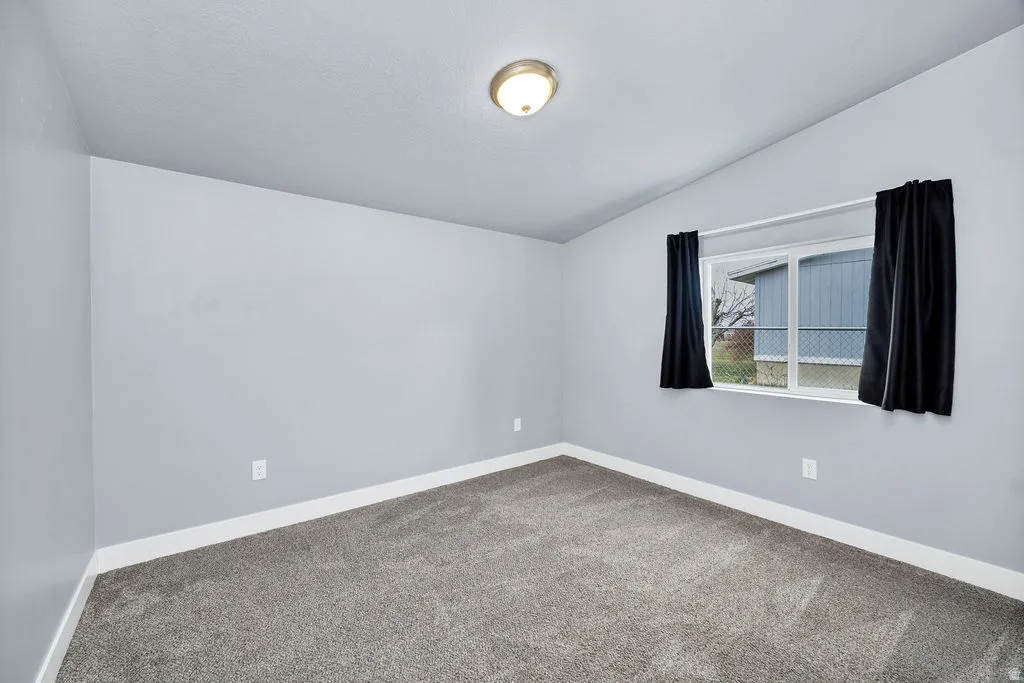 Spare room featuring vaulted ceiling and carpet