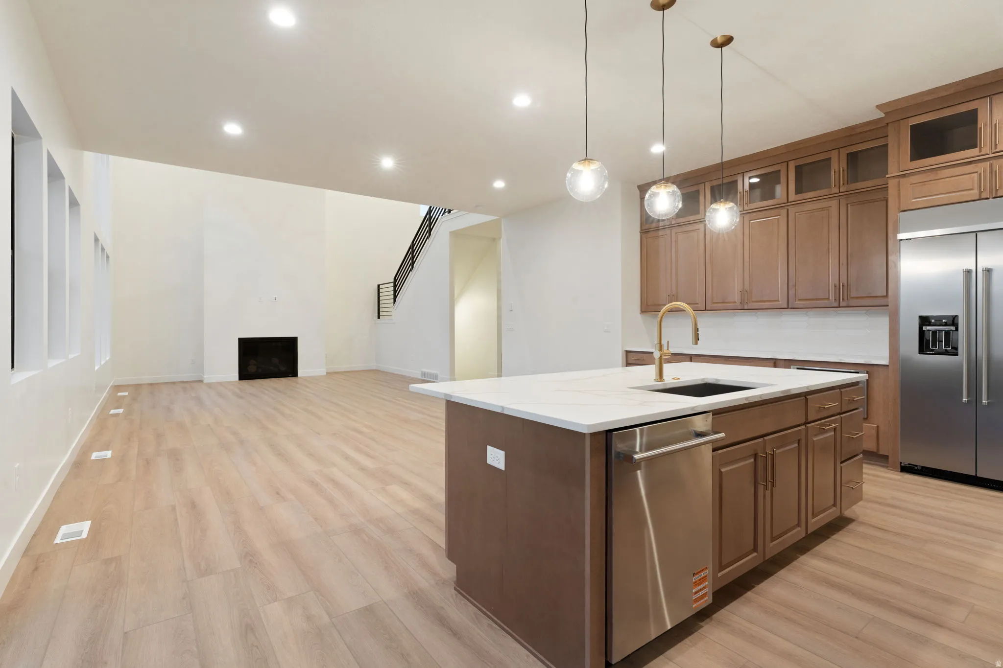 Kitchen featuring an island with sink, open floor plan, stainless steel appliances, pendant lighting, and light wood finished floors