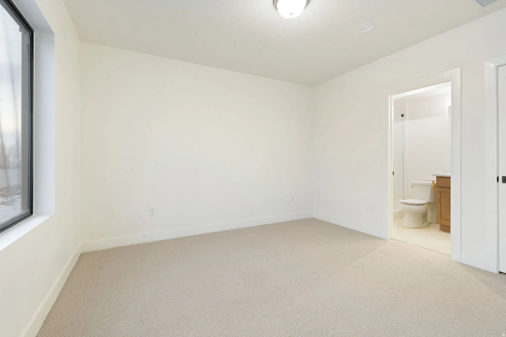 Unfurnished bedroom featuring light colored carpet and ensuite bathroom