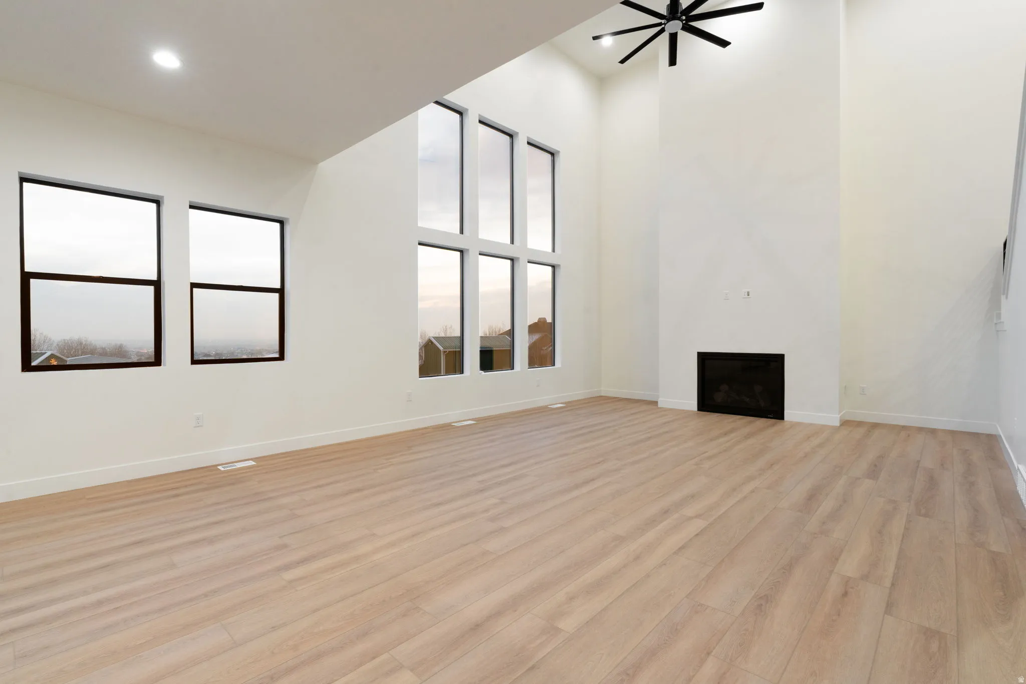 Unfurnished living room with light wood-style floors, a fireplace, a high ceiling, and ceiling fan