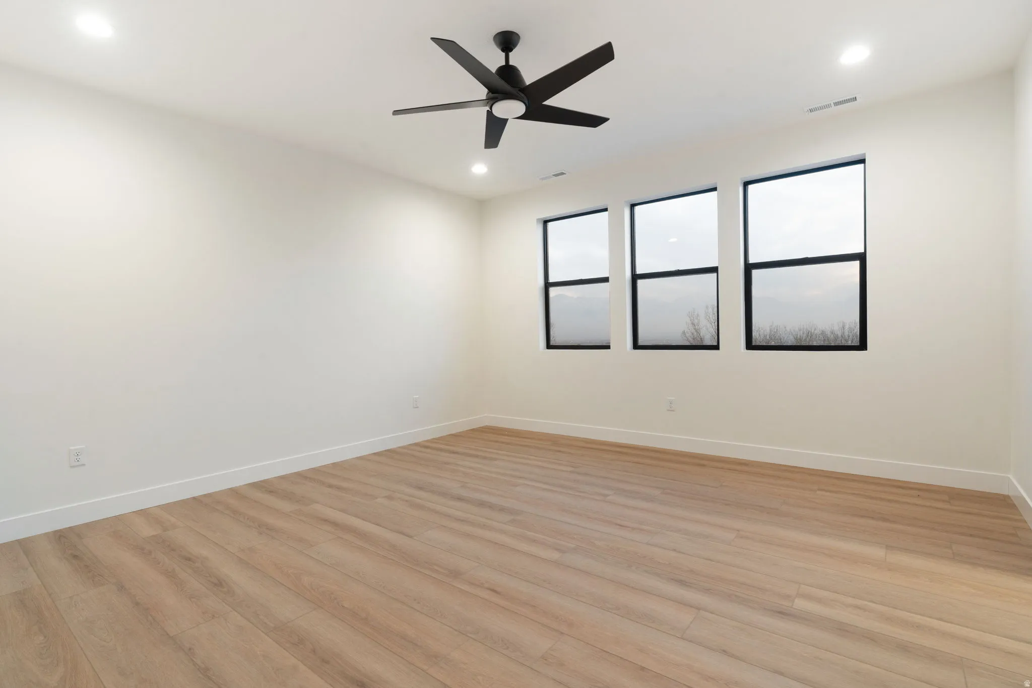 Empty room featuring light wood finished floors, ceiling fan, and recessed lighting