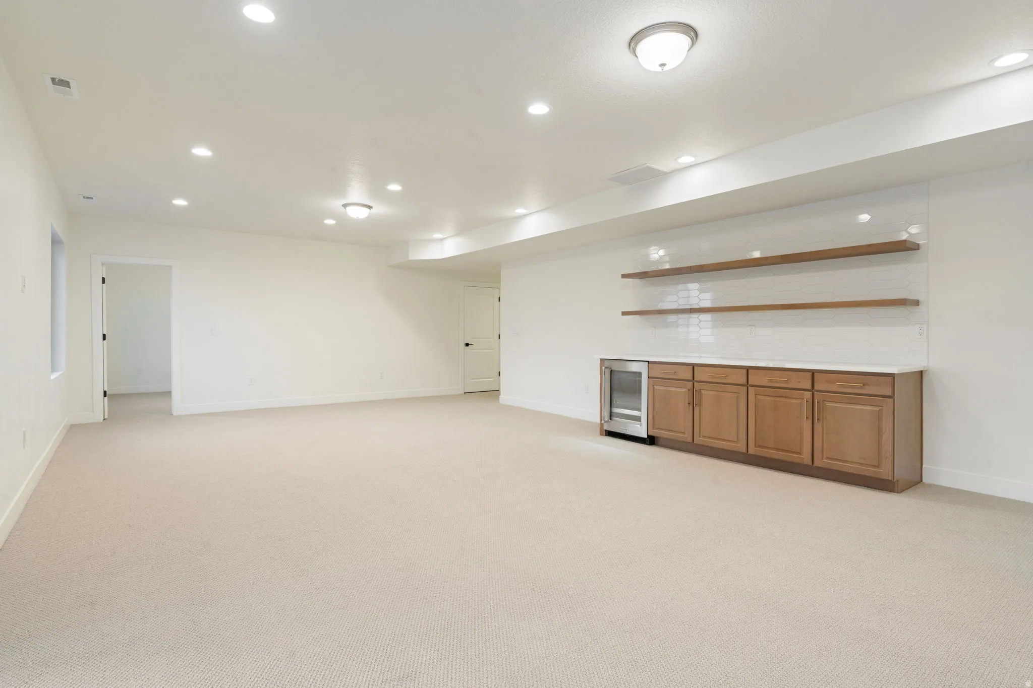 Indoor dry bar with open shelves, light colored carpet, light countertops, wood finish cabinetry, and recessed lighting