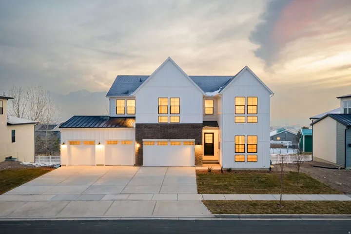 Modern inspired farmhouse with board and batten siding, a standing seam roof, driveway, and a lawn