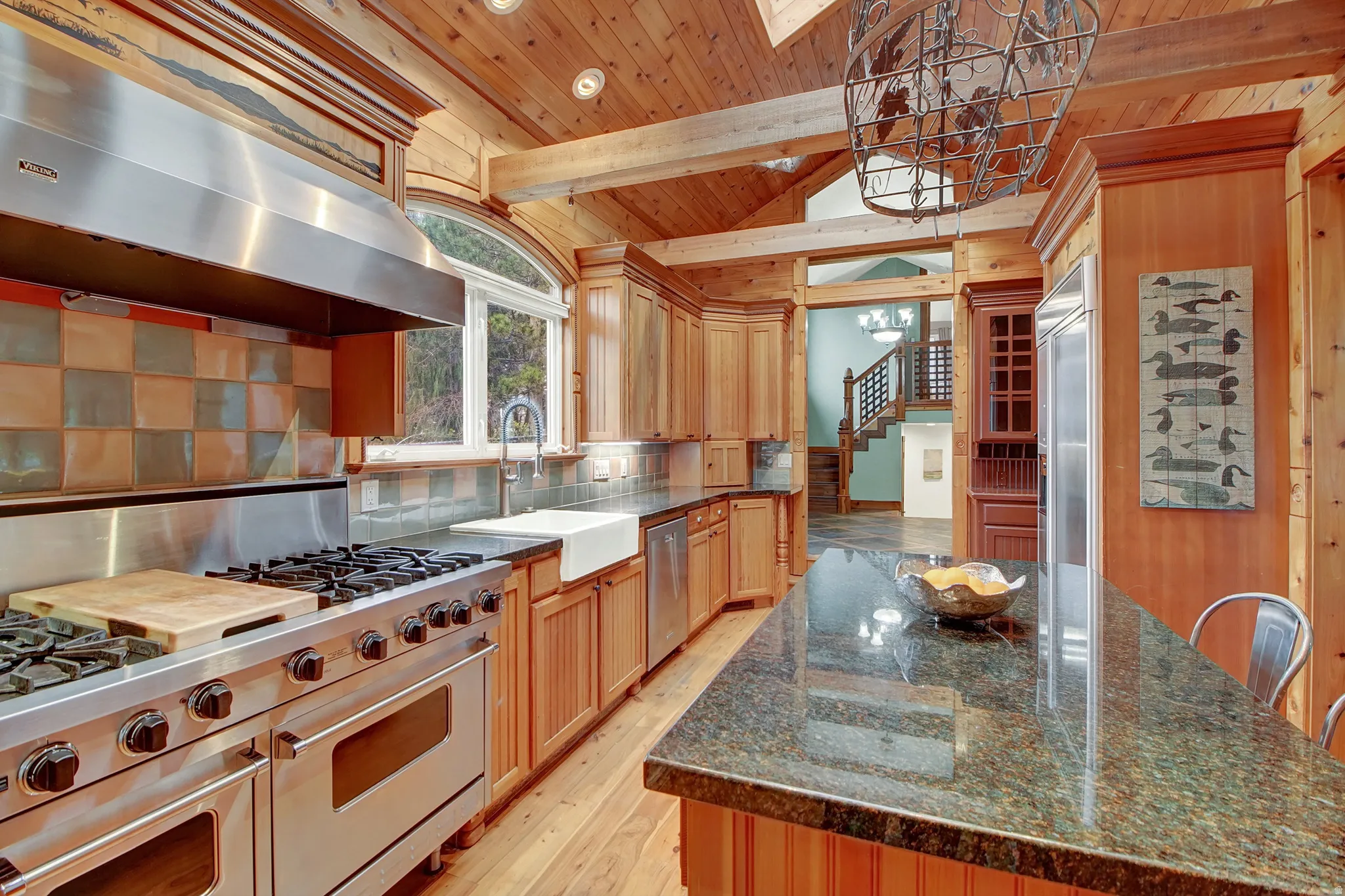 Kitchen featuring high end appliances, range hood, light wood finished floors, suspended lighting, and wooden ceiling