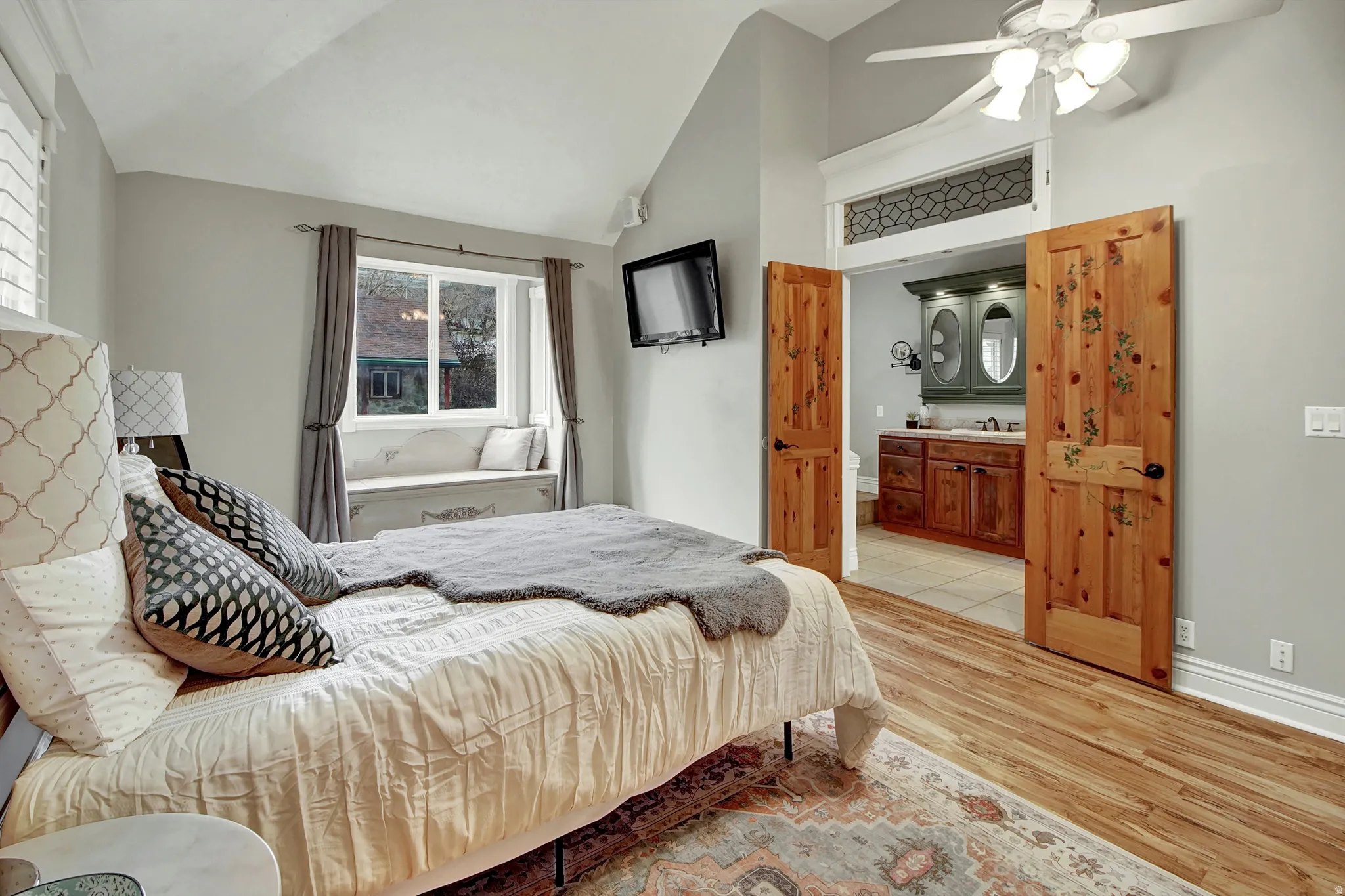 Bedroom with light wood-style flooring, vaulted ceiling, ceiling fan, and ensuite bath